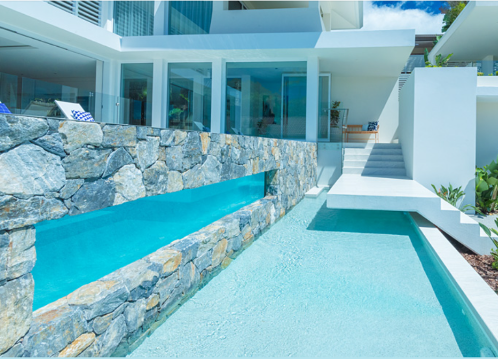 Modern white residence with lap pool featuring horizontal acrylic viewing panel set into natural stone retaining wall